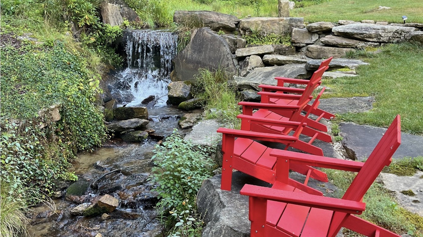 Red Adirondack chairs beside the creek and waterfall at The Green Drake